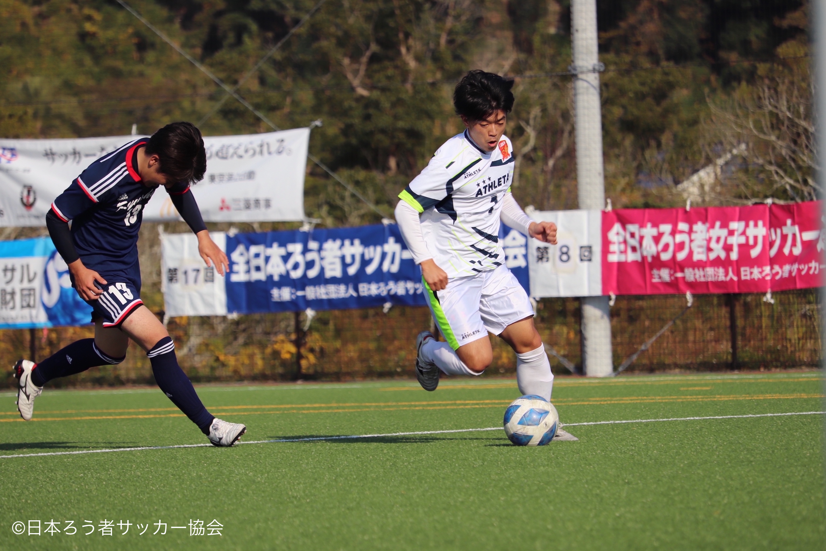 九州選抜対東日本選抜の試合の様子。２人の選手がボールを追いかけている。