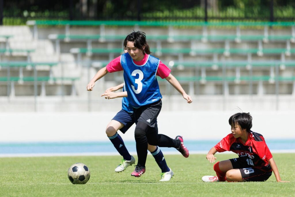 1人の選手が転んでおり、他2人の選手がボールを追いかけている様子